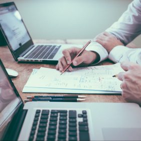 person holding pencil near laptop computer